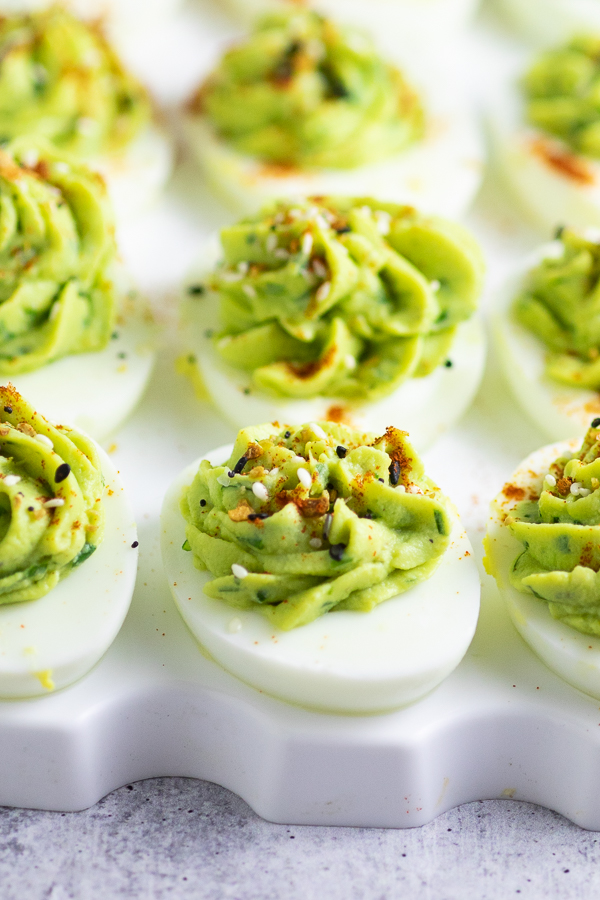 Close up of one of a dozen avocado deviled eggs on a serving tray topped with paprika and everything seasoning