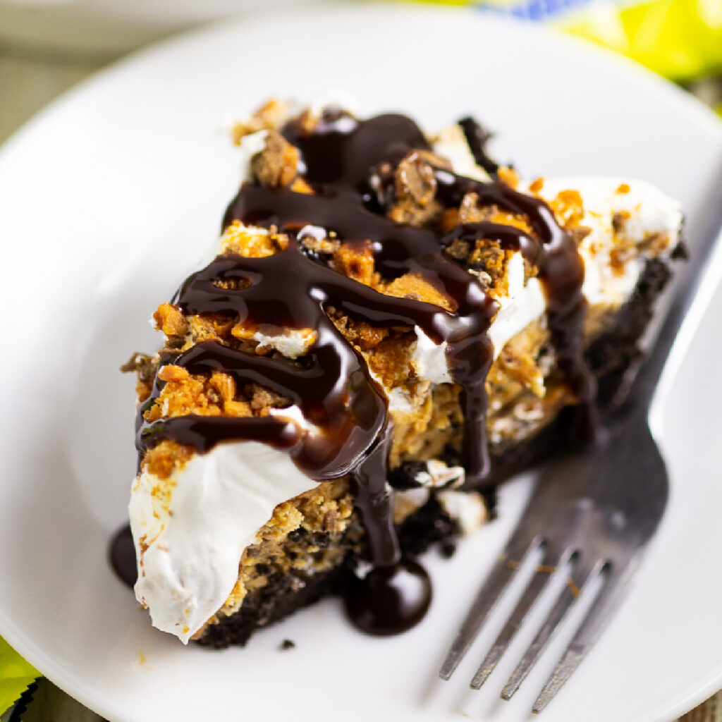 Butterfinger pie topped with dripping chocolate sauce on a small plate next to a fork