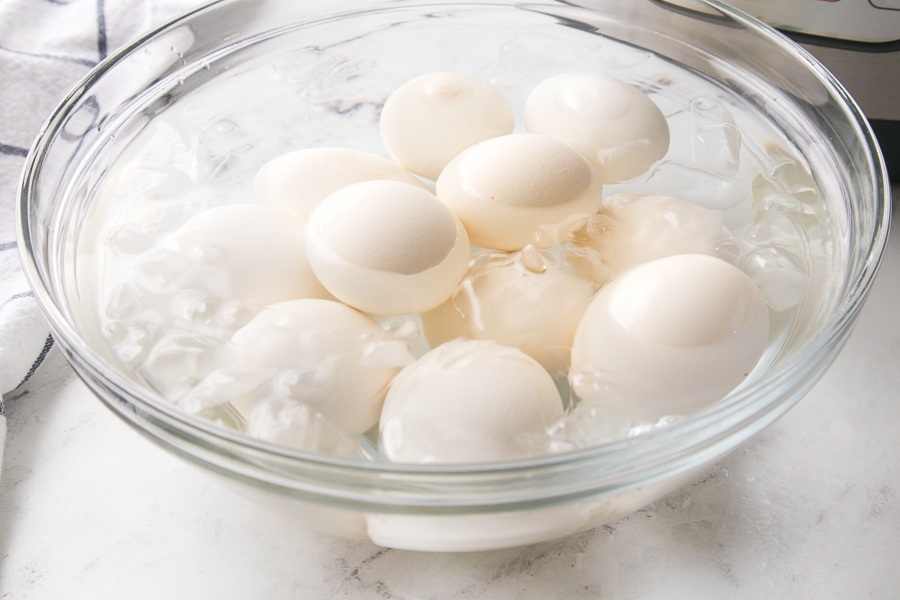 Glass bowl with hard boiled eggs, ice, and water on a marble counter