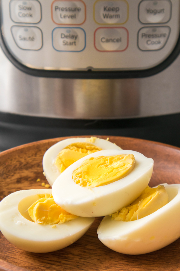 Four hard boiled egg halves sitting on a wooden plate in front of an instant pot