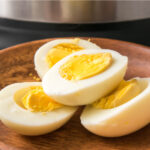 Four hard boiled egg halves sitting on a wooden plate in front of an instant pot