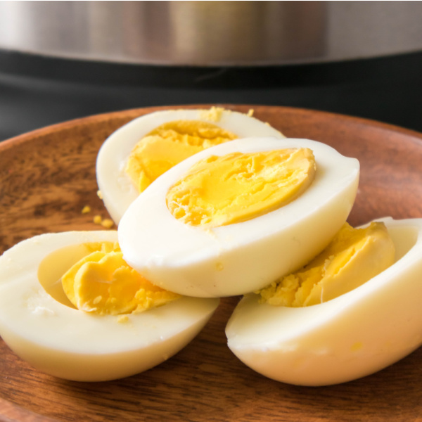 Four hard boiled egg halves sitting on a wooden plate in front of an instant pot