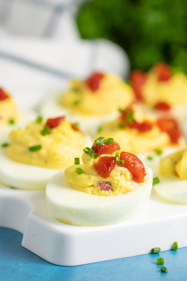 Pimento cheese deviled egg sitting on a deviled egg tray topped with pimentos with fresh parsley in the background