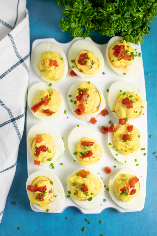 Overhead view of a serving tray with a dozen pimento cheese deviled eggs next to a striped linen and a bunch of fresh parsley