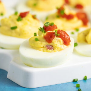 Pimento cheese deviled egg sitting on a deviled egg tray topped with pimentos with fresh parsley in the background