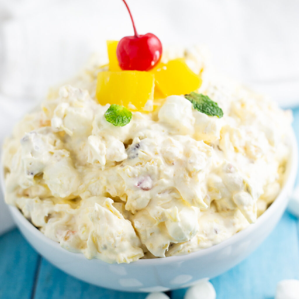 Side view of bowl of Pineapple Fluff topped with pineapple pieces and a cherry.