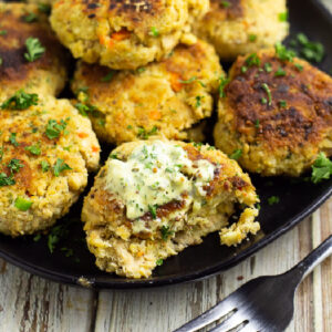 Salmon croquettes on a black matte plate. One is topped with remoulade and a bite is taken out on a rustic wood backdrop.