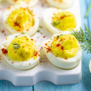 Deviled eggs on an egg platter topped with paprika and fresh dill.