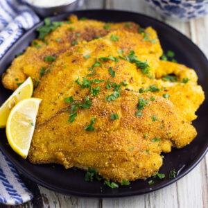 Plate full of pan fried catfish next to lemon wedges next to a linen