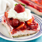 A slice of strawberry pretzel salad on a small plate topped with whipped cream and a fresh strawberry.