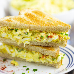 Egg salad sandwich cut diagonally with the halves stacked on top of each other on a plate on a rustic wood background.