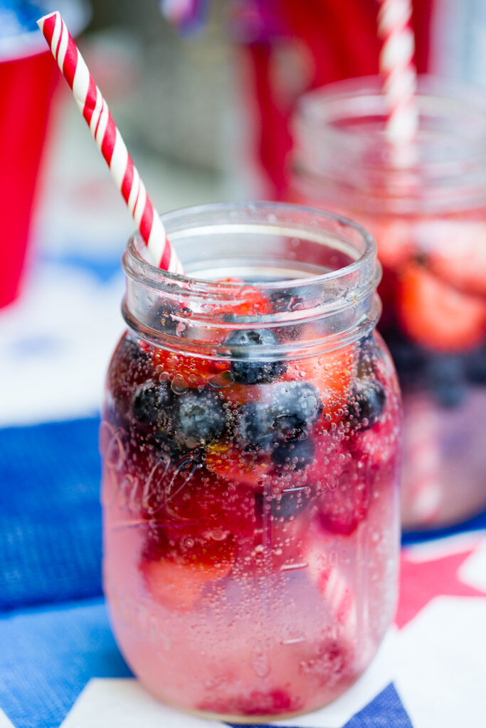 Berry spritzer with frozen strawberries and blueberries and a red striped straw in a mason jar.