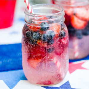 Berry spritzer with frozen strawberries and blueberries and a red striped straw in a mason jar.