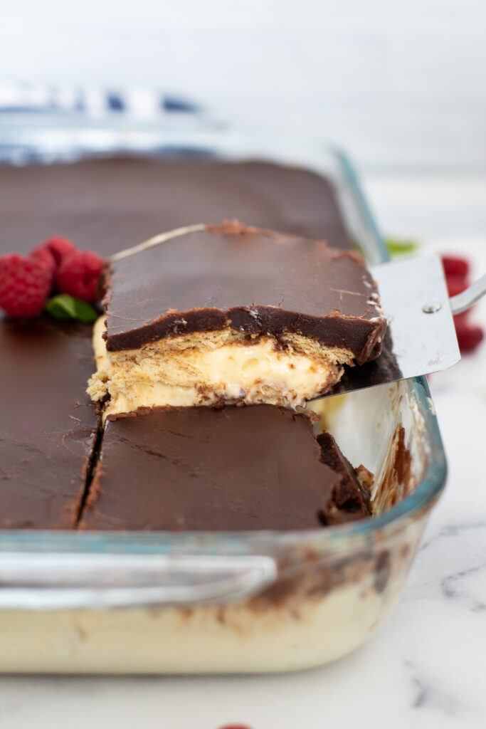 A slice being lifted out of a chocolate eclair cake topped with ripe raspberries