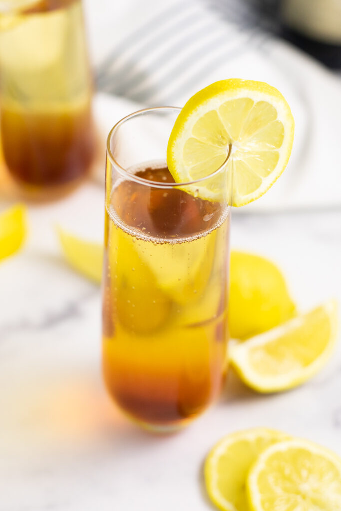 Angled overhead view of an Earl Grey Spritzer in a champagne flute garnished with a lemon slice and fresh lemon wedges scattered around it.