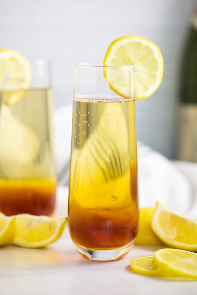Earl Grey spritzer in a champagne flute garnished with a lemon slice with lemon wedges scattered around and a second glass behind.