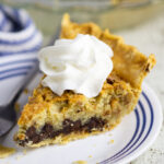 Slice of Kentucky Derby Pie topped with whipped cream on a small plate next to a fork