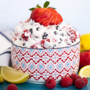 Berry cheesecake salad topped with a sliced strawberry next to a lemon wedge and fresh raspberries