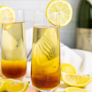 Earl Grey spritzer in a champagne flute garnished with a lemon slice with lemon wedges scattered around and a second glass behind.