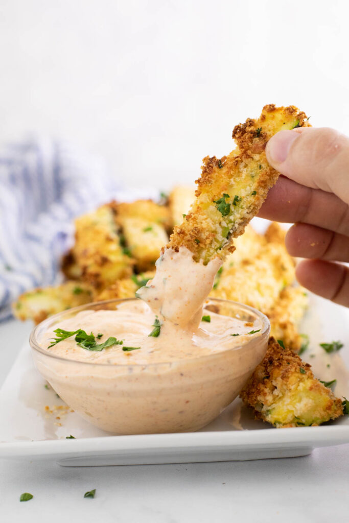 Air fryer zucchini fries being dipped into a sauce in a small glass bowl
