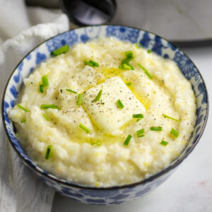 A small bowl full of crockpot grits topped with melting butter, fresh chopped chives, and black pepper