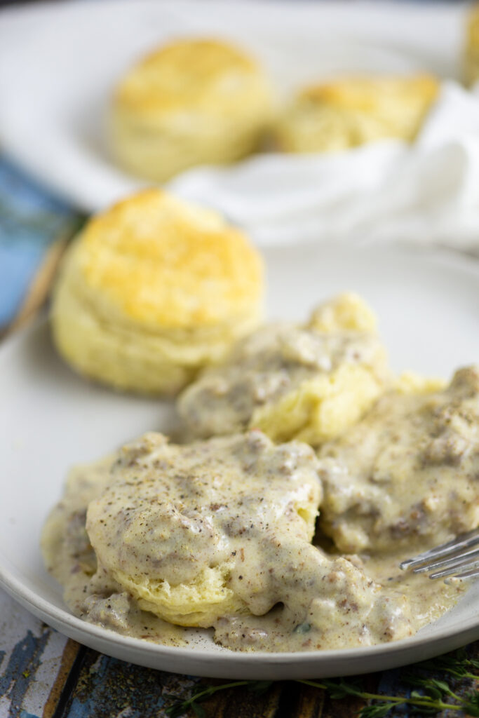 Half a biscuit smothered in sawmill gravy with pork sausage and topped with black pepper with whole biscuits in the background