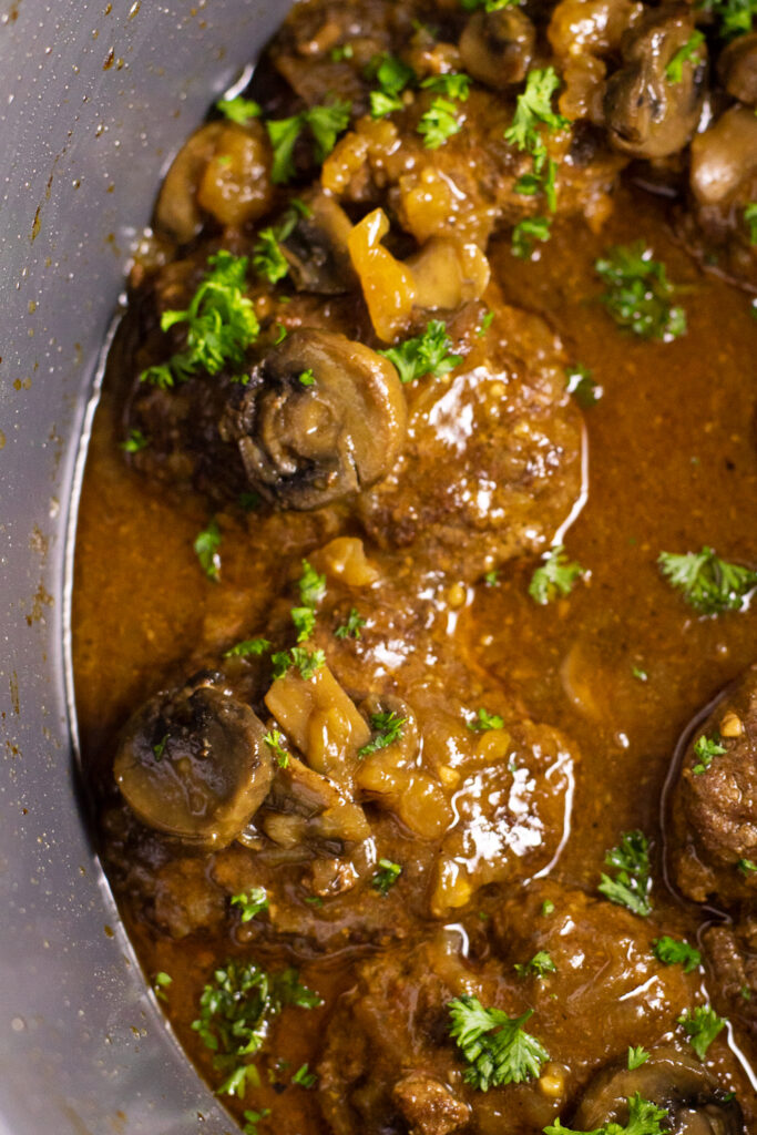 Close up of salisbury steak patties in mushroom and onion gravy topped with fresh chopped parsley all in the crock of a slow cooker