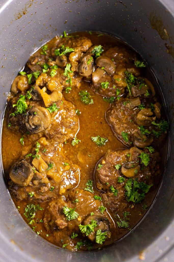 Slow cooker salisbury steak patties in mushroom and onion gravy topped with fresh chopped parsley all in the crock of a slow cooker