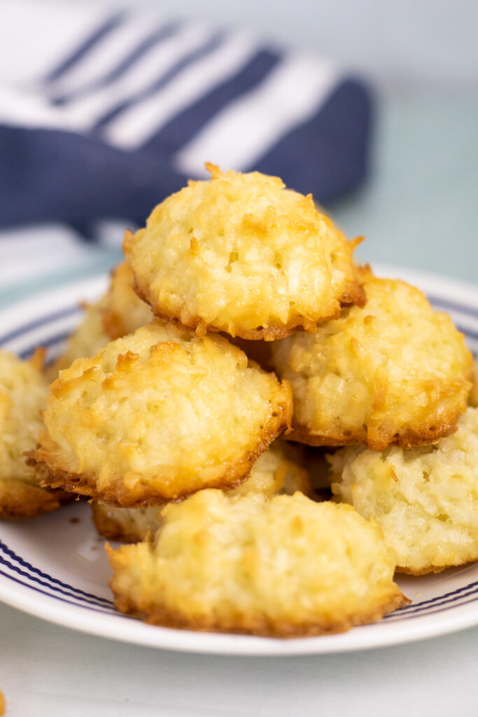 Golden coconut macaroons stacked on a small plate with a linen napkin behind.