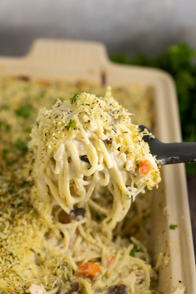 A spoon taking a large scoop of turkey tetrazzini from a casserole dish
