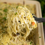 A spoon taking a large scoop of turkey tetrazzini from a casserole dish