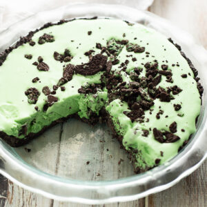 Overhead view of a Grasshopper pie with a slice missing, topped with Oreo crumbles in a glass pie dish