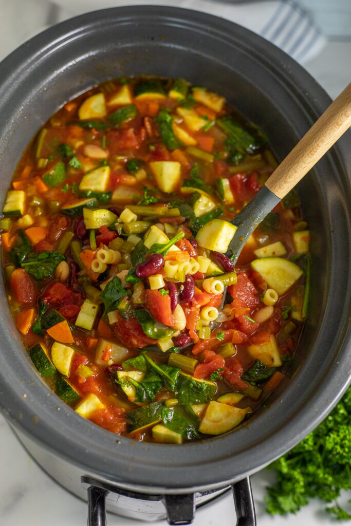 Slow cooker minestrone soup in a large Crockpot with a ladle taking a scoop from the center.