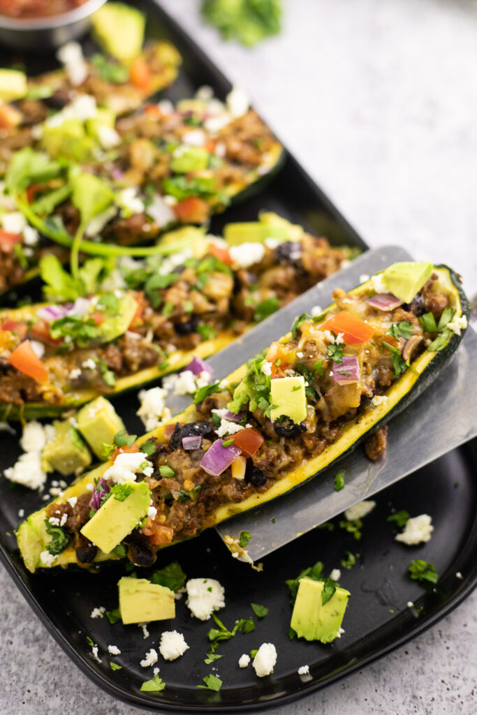 A taco zucchini boat being lifted by a metal spatula off of a black matte plate