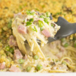 Silicone spoon scooping up ham tetrazzini from a big casserole dish