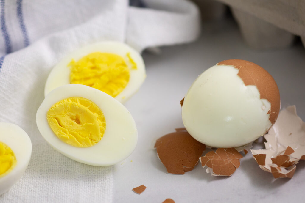A hard boiled egg cut in half on the left and an egg half-peeled on the right with a linen napkin behind