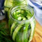 Overhead view into a jar of refrigerator dill pickles sitting on a wooden cutting board.