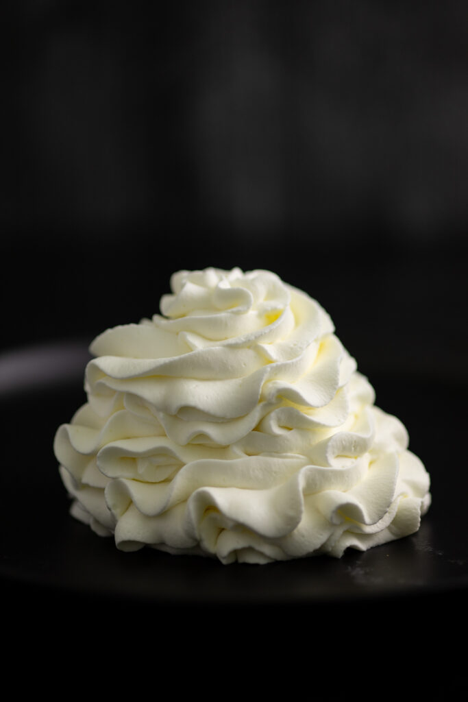 A swirl of piped stabilized whipped cream on a black background.