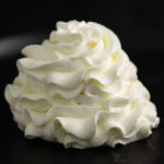 A swirl of piped stabilized whipped cream on a black background.