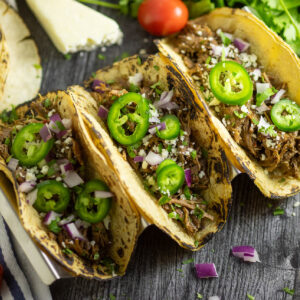 Overhead view of three instant pot barbacoa tacos topped with red onions, jalapeno slices, and fresh chopped cilantro.