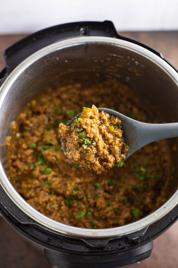 A silicone spoon scooping sloppy joes topped with fresh chopped parsley from an Instant pot.