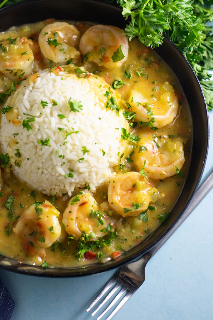 Overhead view of Shrimp etouffee served with white rice in the center in the shape of a half-sphere, topped with fresh chopped parsley sitting next to a fork and a fresh bunch of parsley.