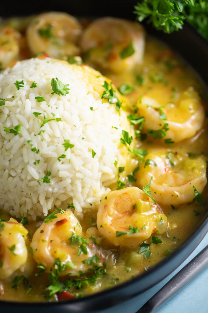 Close up of Shrimp etouffee served with white rice in the center in the shape of a half-sphere, topped with fresh chopped parsley.