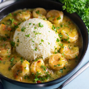 Shrimp etouffee served with white rice in the center in the shape of a half-sphere, topped with fresh chopped parsley.