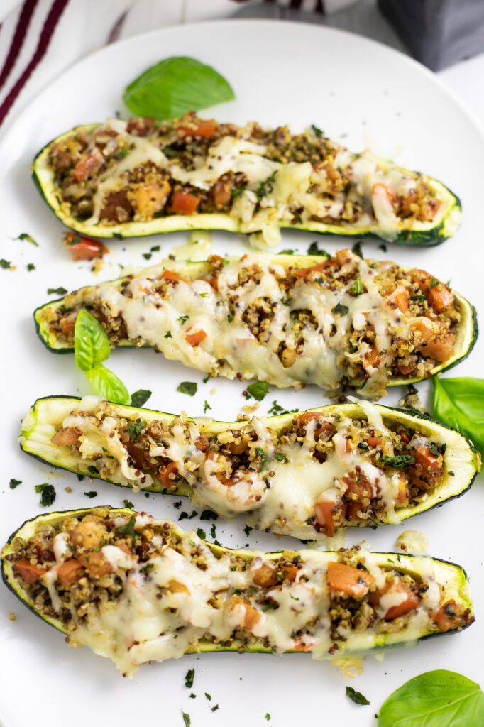 An overhead view of four vegetarian bruschetta zucchini boats surrounded by fresh basil leaves.