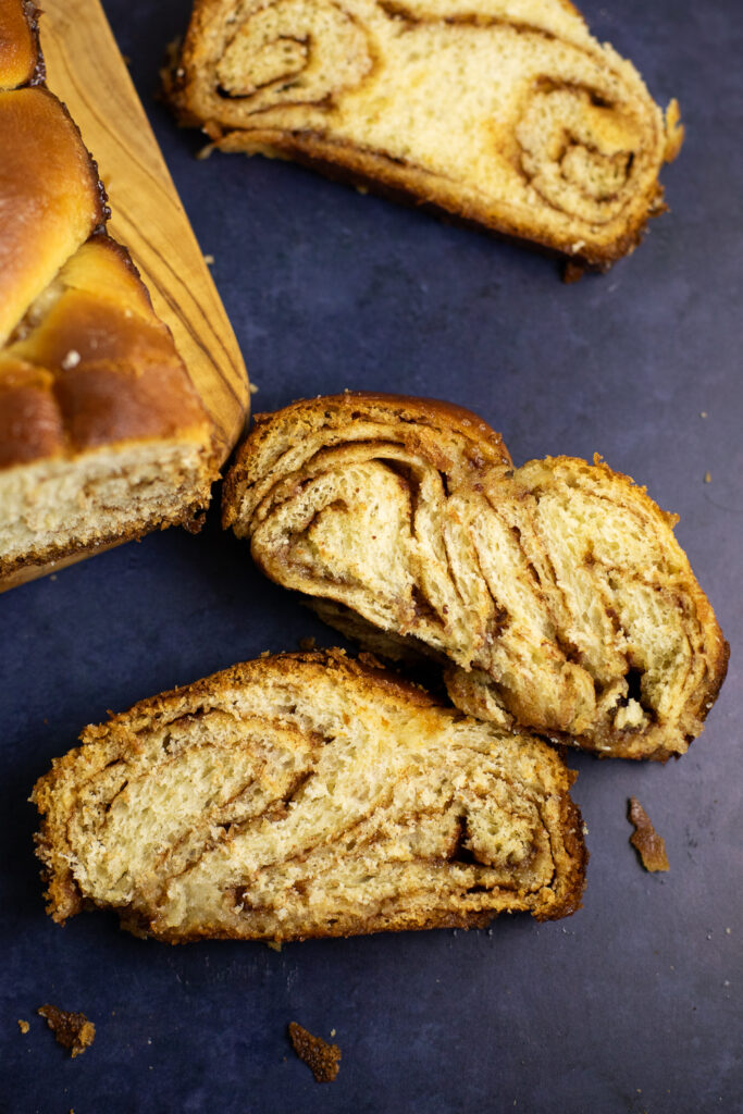 Two slices of cinnamon babka with different swirl patterns next to the remaining loaf on a cutting board.