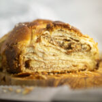 A loaf of cinnamon babka on a small cutting board showing just the end where pieces have already been cut off, exposing the swirls inside.