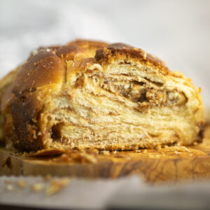 A loaf of cinnamon babka on a small cutting board showing just the end where pieces have already been cut off, exposing the swirls inside.