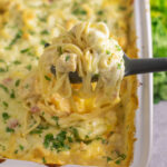 A silicone spoon scooping out a large cheesy portion of Rotel chicken spaghetti topped with fresh cilantro from a large casserole dish.