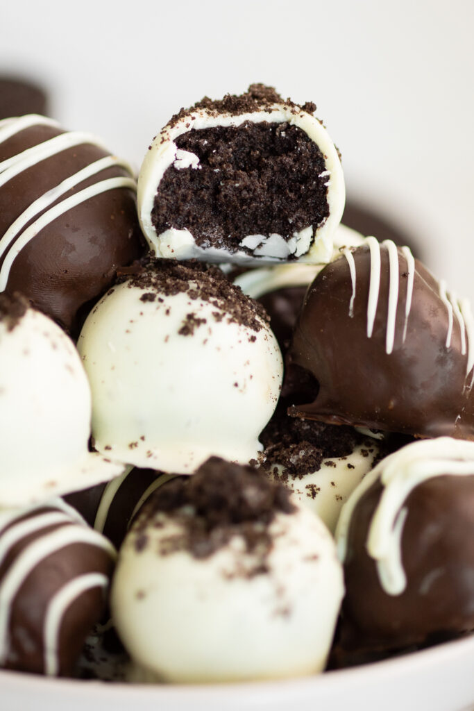 A pile of Oreo truffles with the top, white chocolate covered truffle with a bite taken out of it.